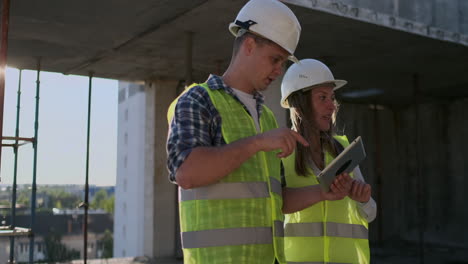 Professional-engineers-in-safety-vests-and-helmets-working-with-digital-tablet-and-blueprints